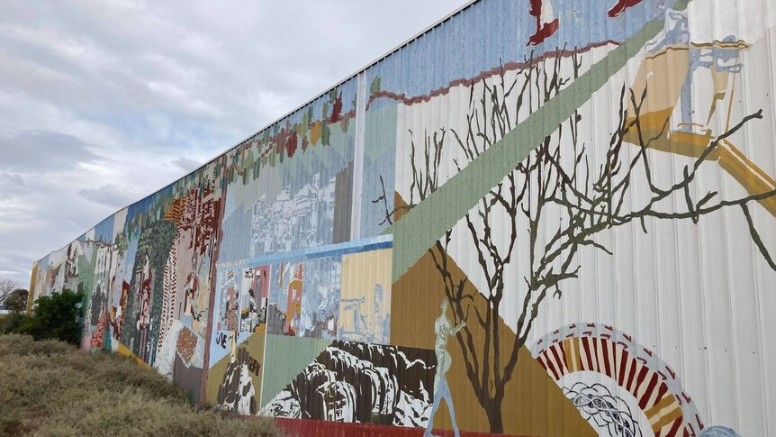 A large wall covered with an art mural sits behind some shrubs. 