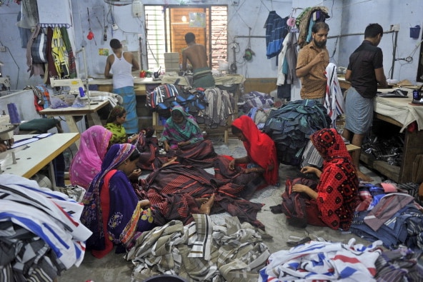 A group of workers sort clothes on the floor of a factory.