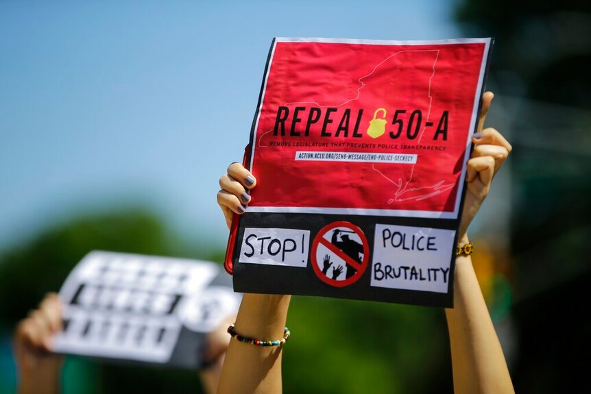 A read sign that reads "repeal 50-A" is held by a person in crowd of other protesters.