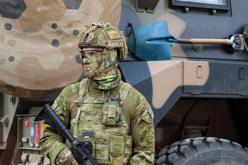 A soldier from 7RAR stands guard in front of a Bushmaster.