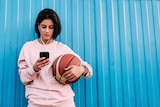 A woman looks at her smartphone against a blue fence.