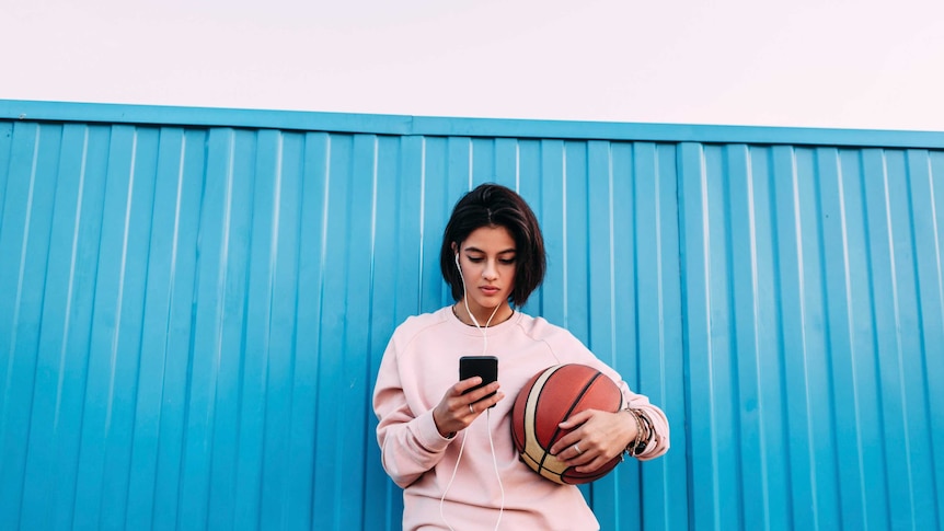 A woman looks at her smartphone against a blue fence.