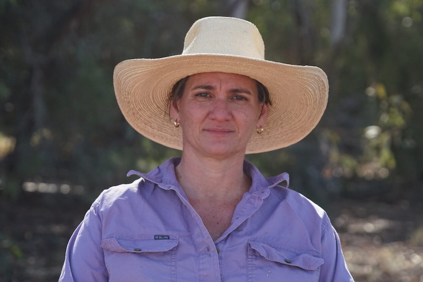 Woman wearing a large hat smiles wearily 