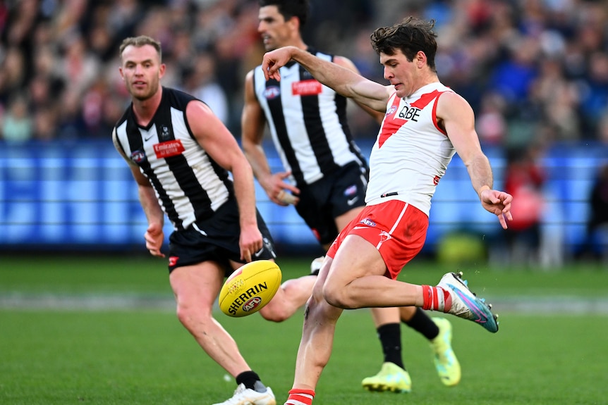 A Sydney Swans player gets ready to swing his left leg through the ball as two Collingwood players close in.