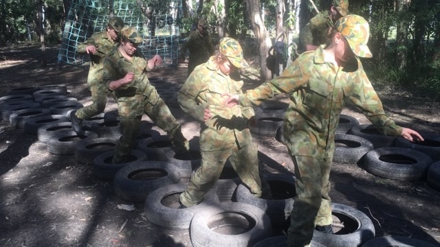 adolescents in army camouflage uniforms jump through tyres in the bush