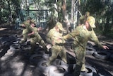 adolescents in army camouflage uniforms jump through tyres in the bush