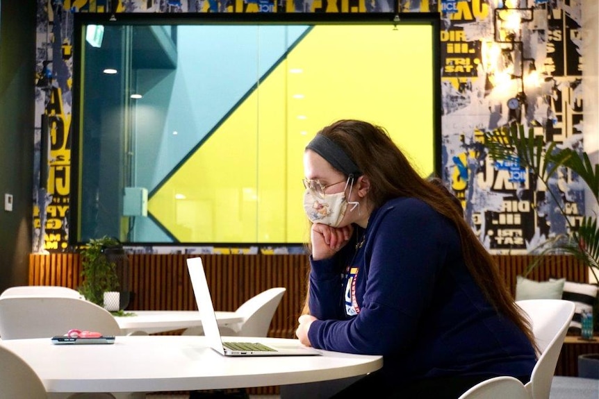 Rebekah wearing a blue jumper, with her head resting on her hand working on a laptop computer. 