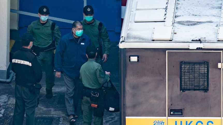 Four Chinese police (dressed in green shirts), lead a prisoner (dressed in blue jacket) to a prison van