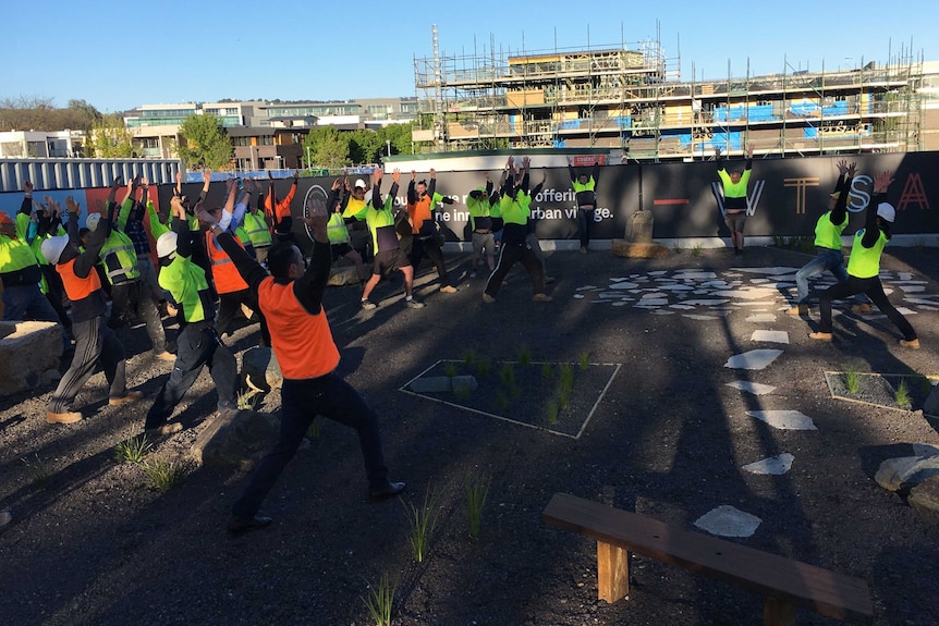 High-vis clad workers do yoga poses.