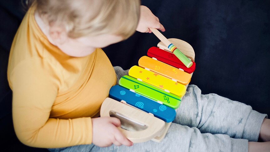 Toddler playing a wooden toy xylophone.