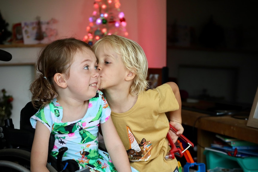 A young blonde kid kisses his sister in their living room.