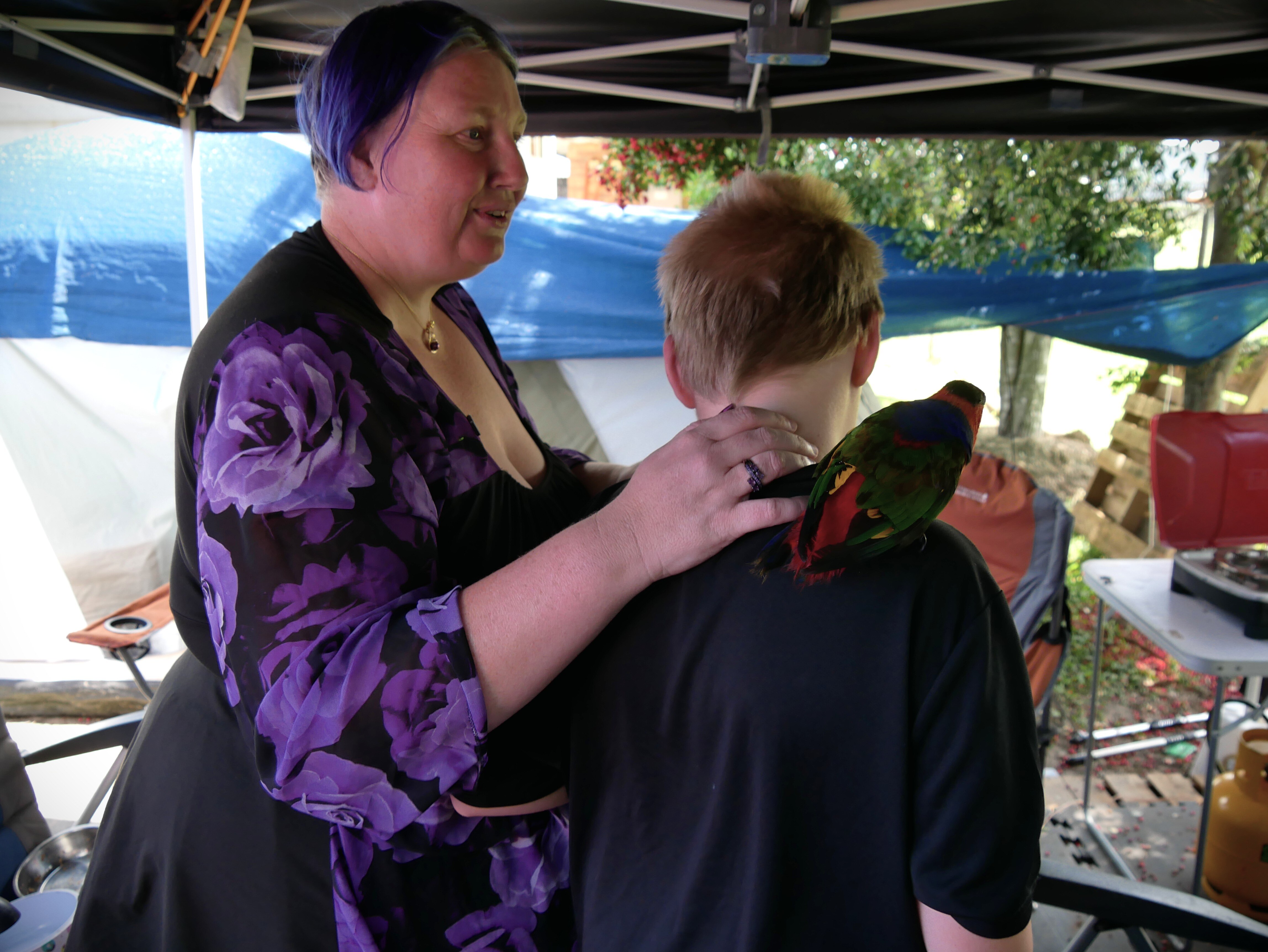 Una mujer rodea a su hijo con el brazo mientras un pájaro se posa en su hombro