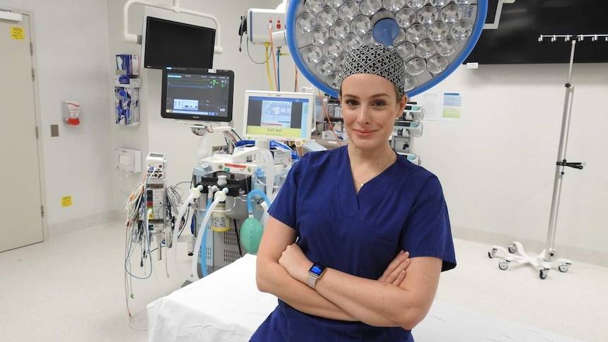 A surgeon in scrubs stands in an operating room.