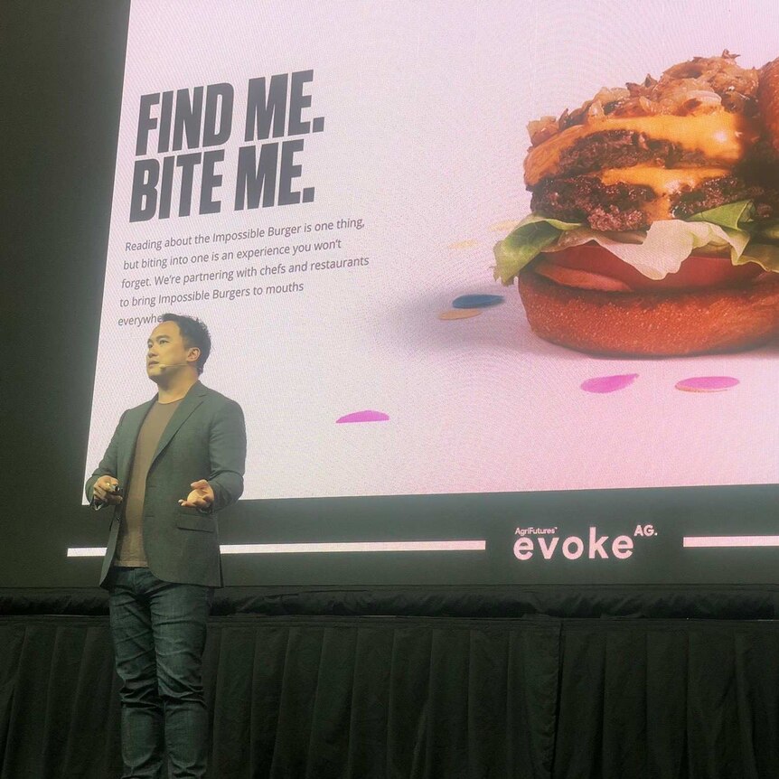 a man standing on a stage infront of a screen with a hamburger on it.
