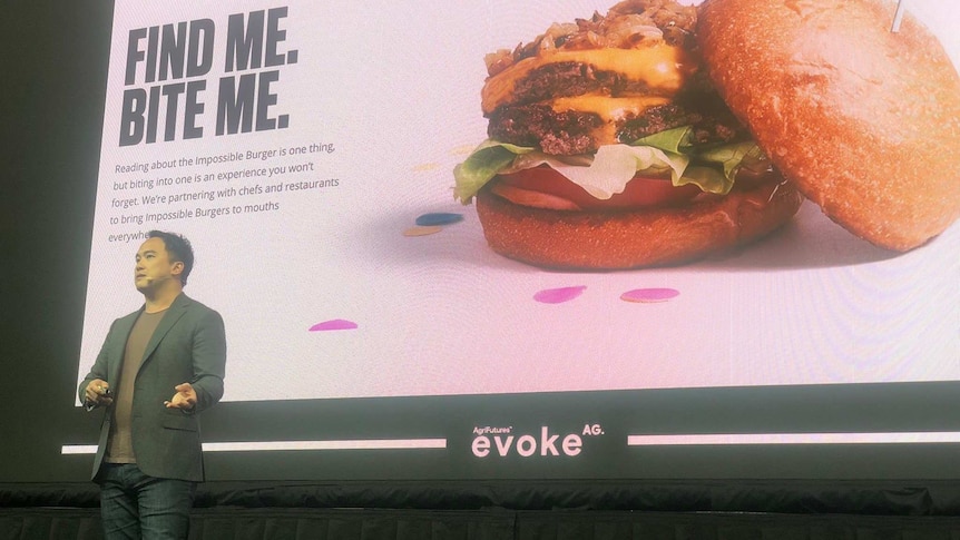 a man standing on a stage infront of a screen with a hamburger on it.