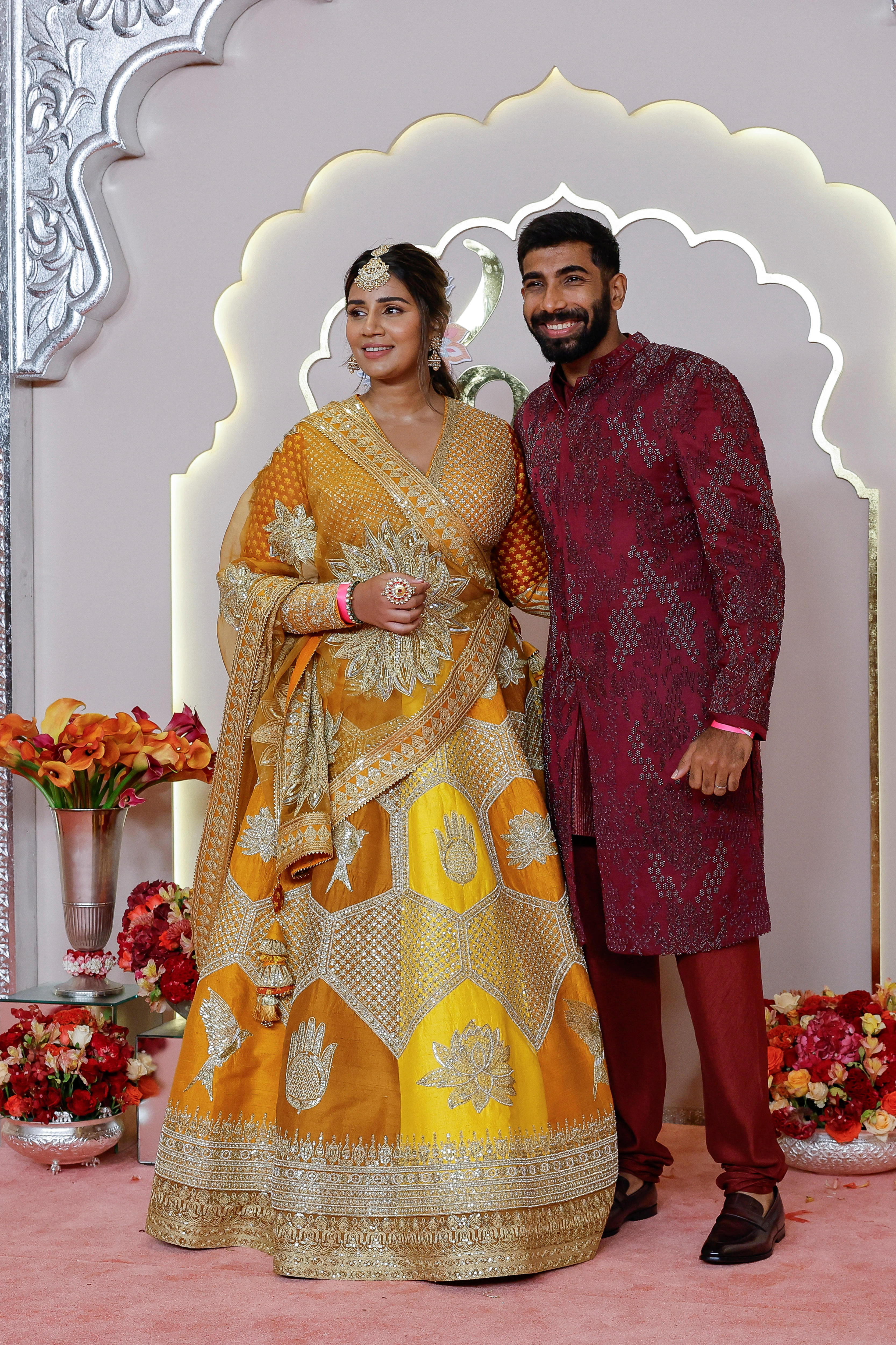 Sanjana Ganesan wears a yellow and orange gown with long sleeves Jasprit Bumrah wears a maroon tunic and pants