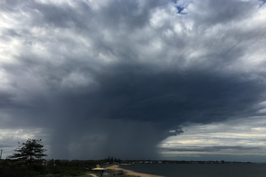 A wide angle image showing dark storm clouds and a rain band with a beach in the foreground.
