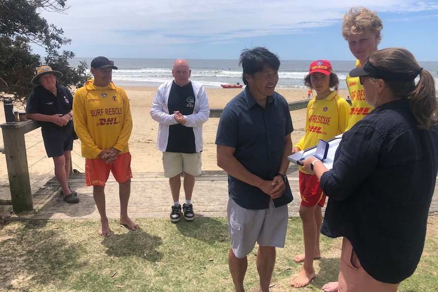 A man smiles as he speaks with surf life savers.