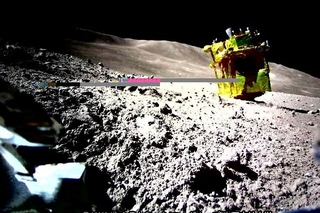 A yellow spacecraft with a pink line at the end of it surrounded by a bunch of space rocks on the moon.