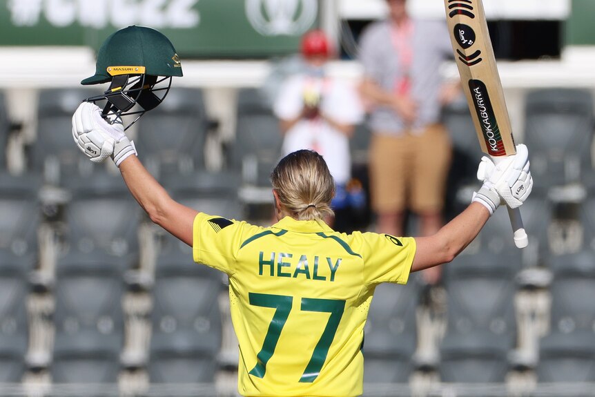 Alyssa Healy, seen from behind, raises her bat in one hand and helmet in the other during the ODI World Cup final.