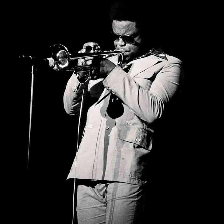 A monochrome photo Freddie Hubbard on-stage playing his trumpet into a mic