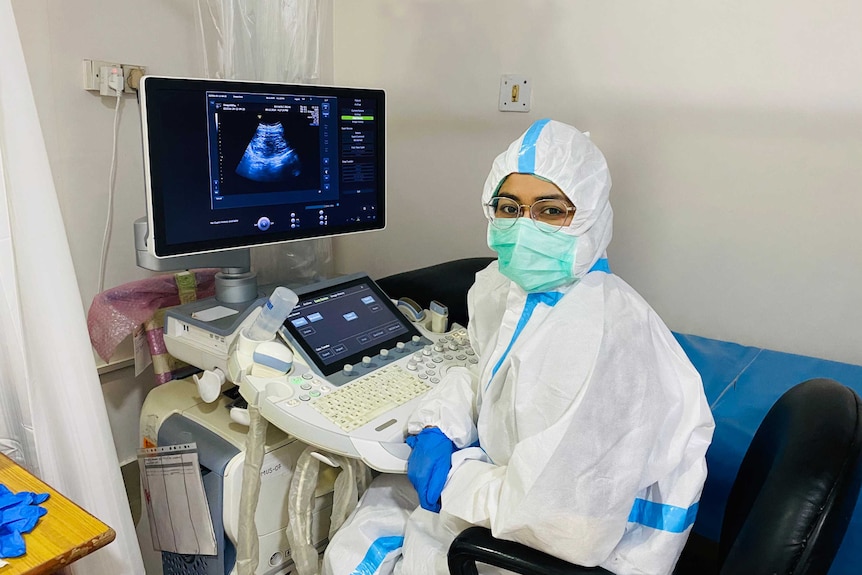 A woman in glasses in a facemask and full PPE sitting at a computer