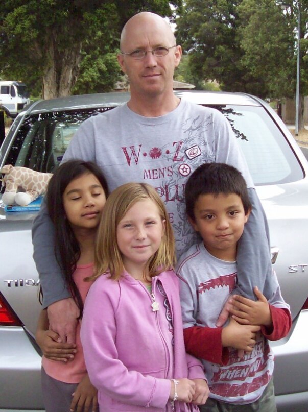 Man with three children in front of a car.