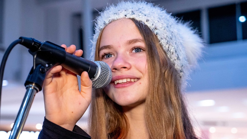 A young girl smiling holding a microphone near hear face.