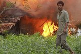 An ethnic Rakhine man holds homemade weapons as he stands in front of a burning house.