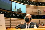 A man wearing a mask listens as Ukraine's President Volodymyr Zelenskyy gives a speech via video link.