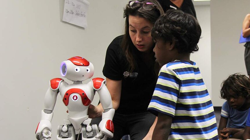 A year five student crouches before a humanoid robot which responds to what you say.
