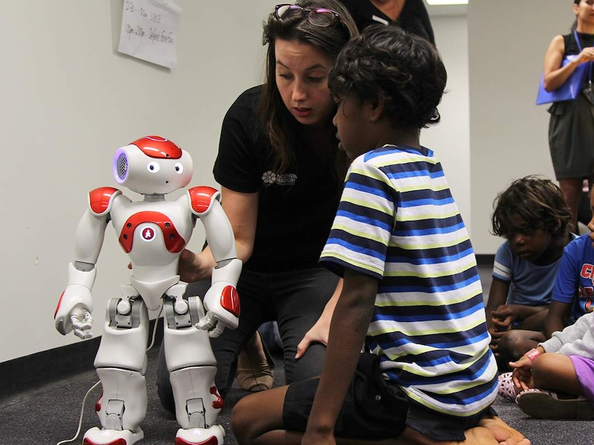 A year five student crouches before a humanoid robot which responds to what you say.