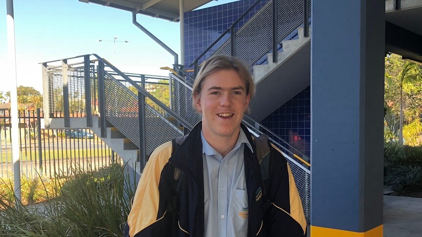 A smiling teenage boy standing in school uniform near stairs of a school building