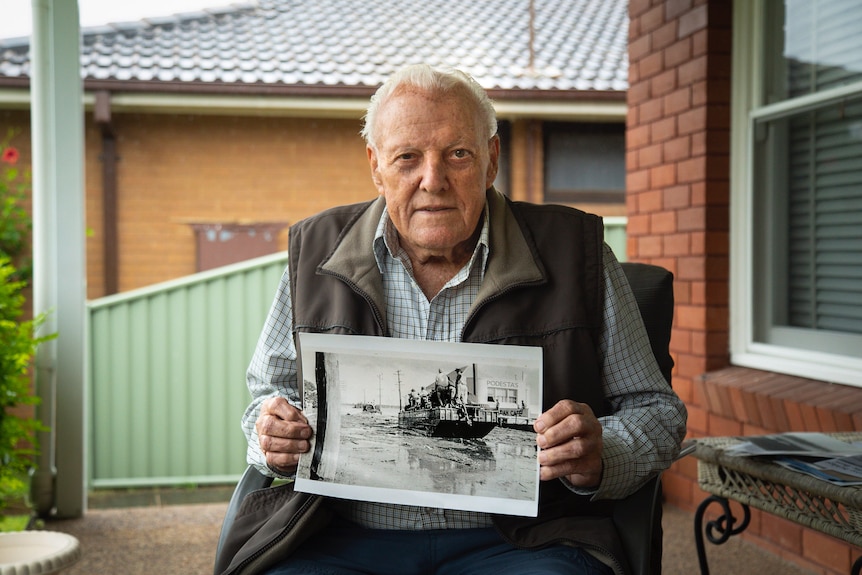 A man holds a black and white picture of a boat on water.