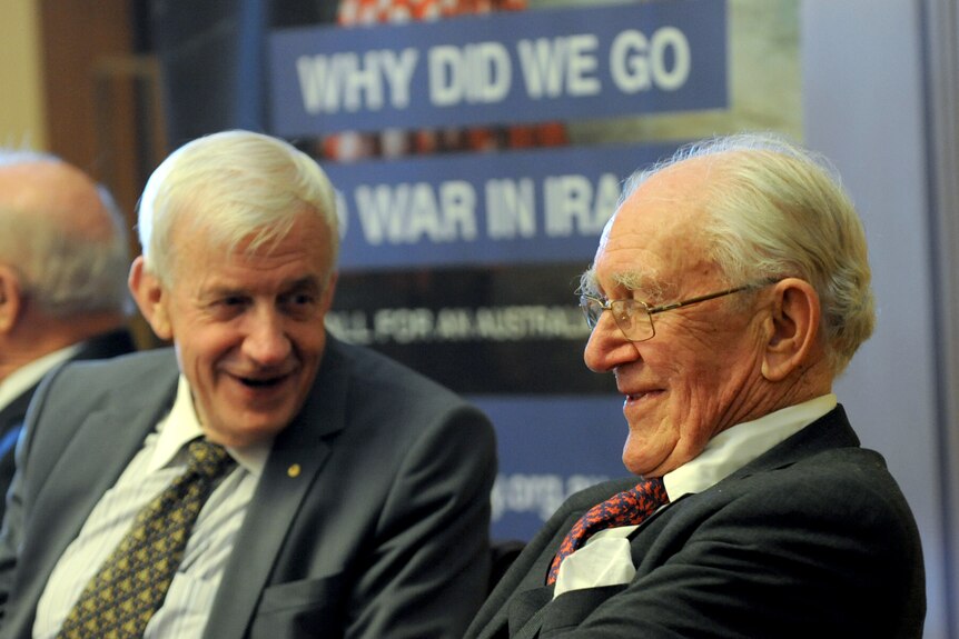 Paul Barratt and Malcolm Fraser sharing a laugh in front of a sign which states: Why did we go to war in Iraq?