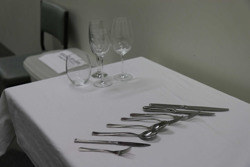 Different wine and water glasses, along with knives, forks and spoons, sit neatly arranged on a table with white tablecloth.