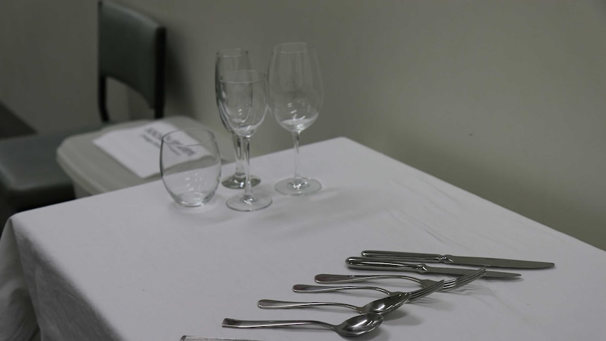 Different wine and water glasses, along with knives, forks and spoons, sit neatly arranged on a table with white tablecloth.