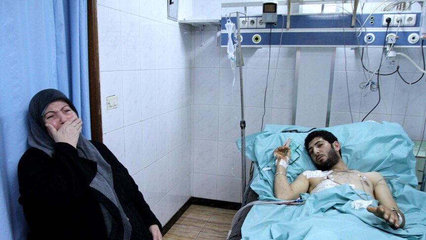 A woman cries as she sits by the hospital bed of a man wounded in violent clashes in Latakia
