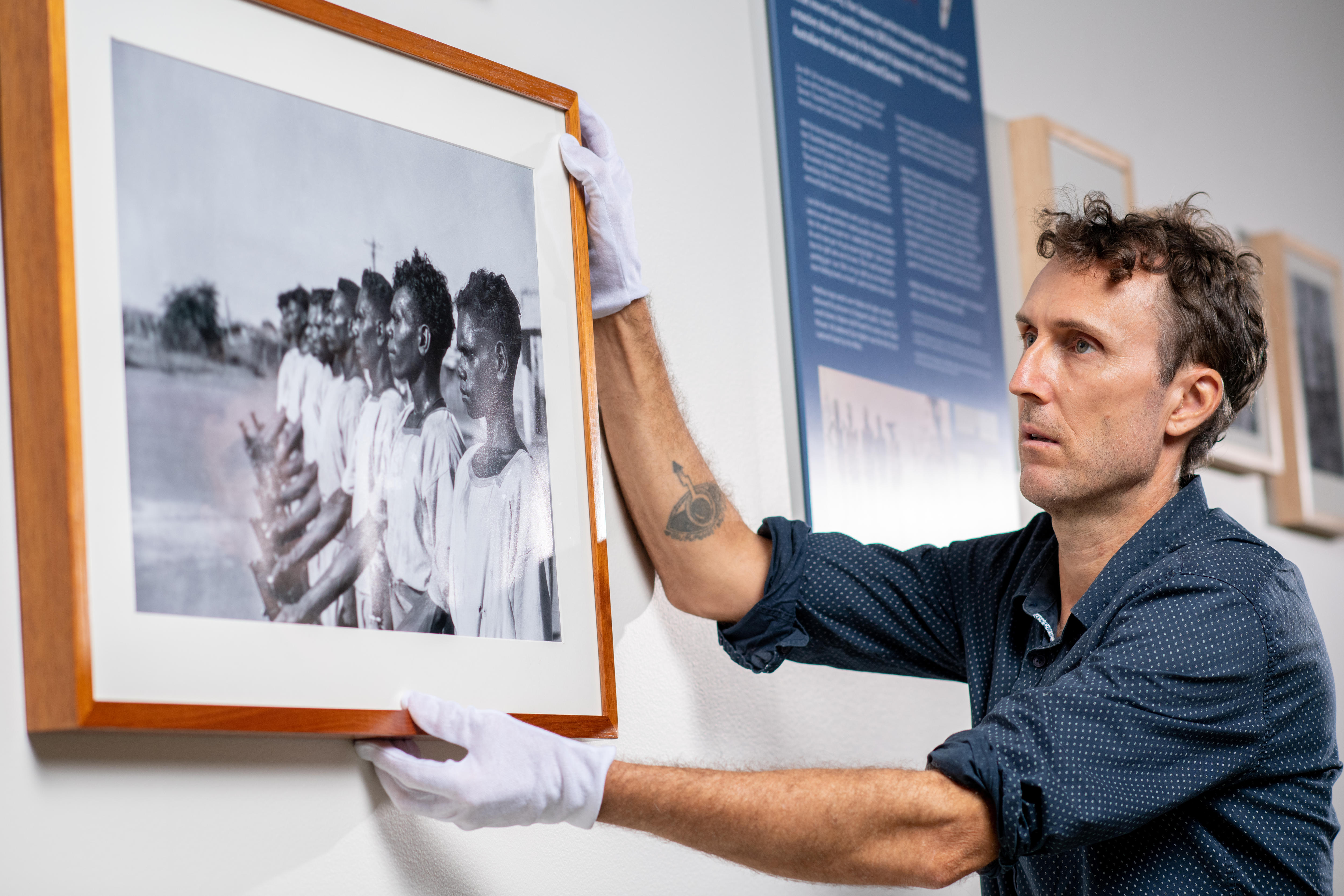 Man in white museum gloves hangs a picture on a wall.