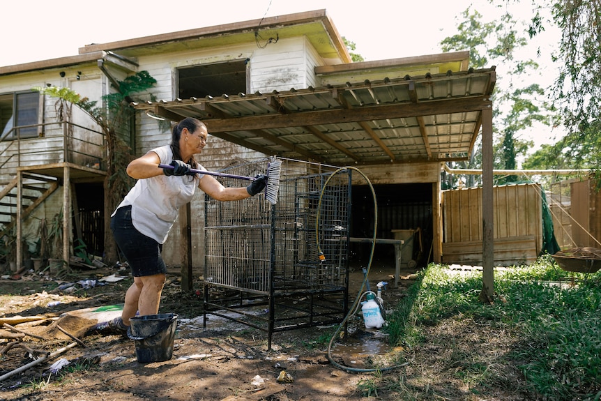 Cheryl cleaning a bird cage with broom in dirty yard