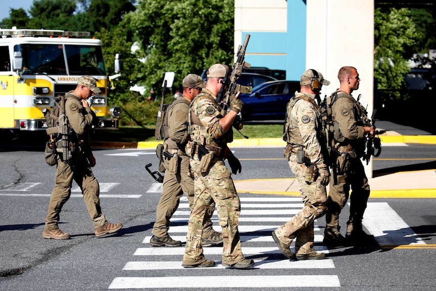 Special tactical police carrying high-powered weapons walk along a street.