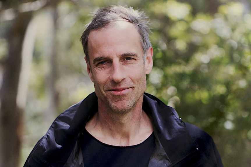 A middle-aged man with short grey hair smiling and wearing a black shirt and jacket.