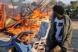 An asylum seeker walks past a burning makeshift shelter.