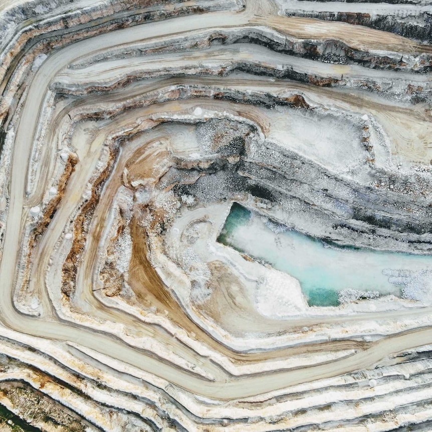 A photo of a mining site taken from an aerial view with white layers of land and blue pools at the bottom of the pit.