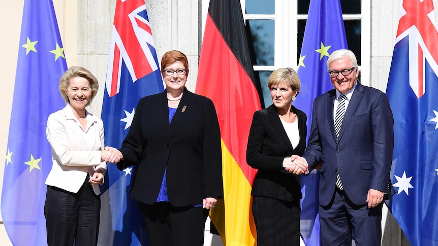 The Australian and German Defence Ministers and Foreign Ministers stand in front of flags shaking hands during Berlin talks.