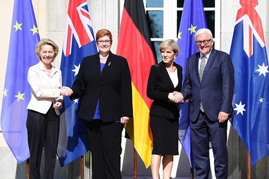 The Australian and German Defence Ministers and Foreign Ministers stand in front of flags shaking hands during Berlin talks.
