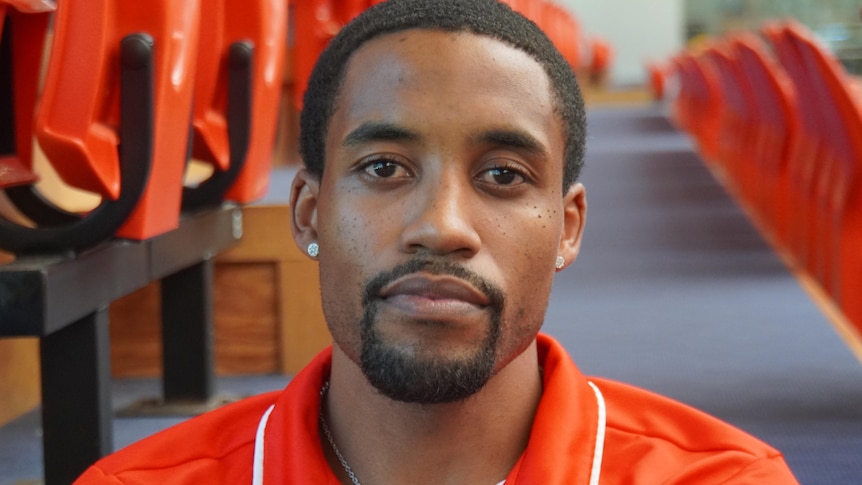 Head shot of Bryce Cotton wearing an orange top and looking straight in to the camera. 