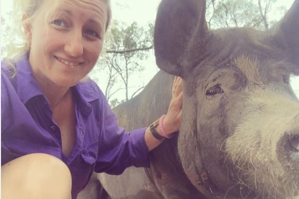 A close-up of a woman crouching next to a big grey and white pig.