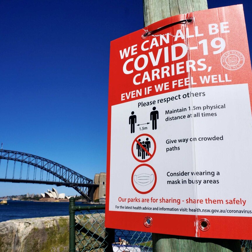 A COVID-19 sign on a pole next to Sydney Harbour.