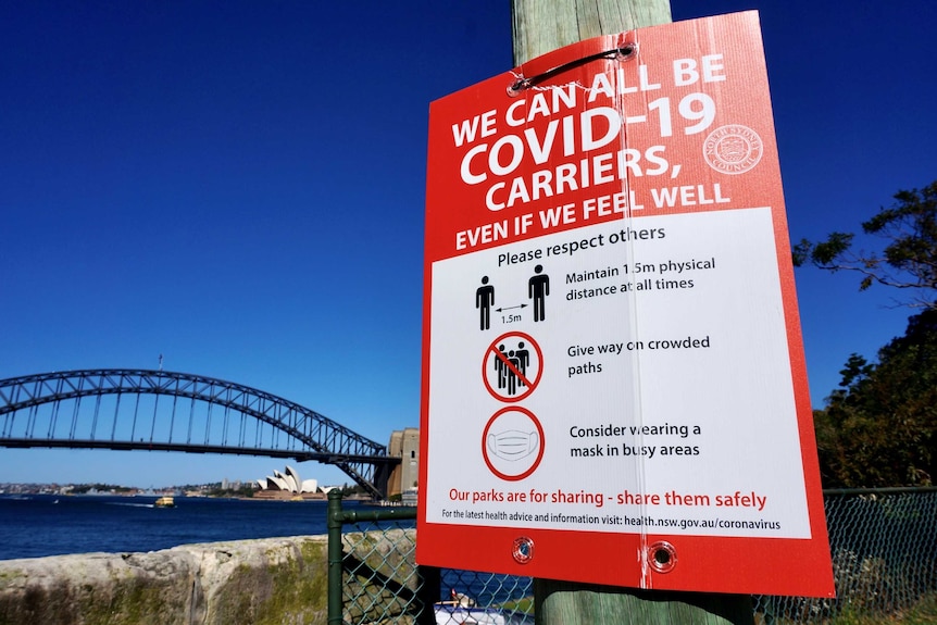A COVID-19 sign on a pole next to Sydney Harbour.